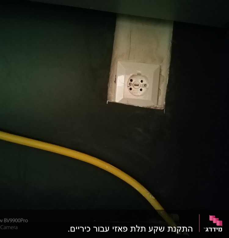 שקע חשמל עם כבל צהוב על קיר כהה